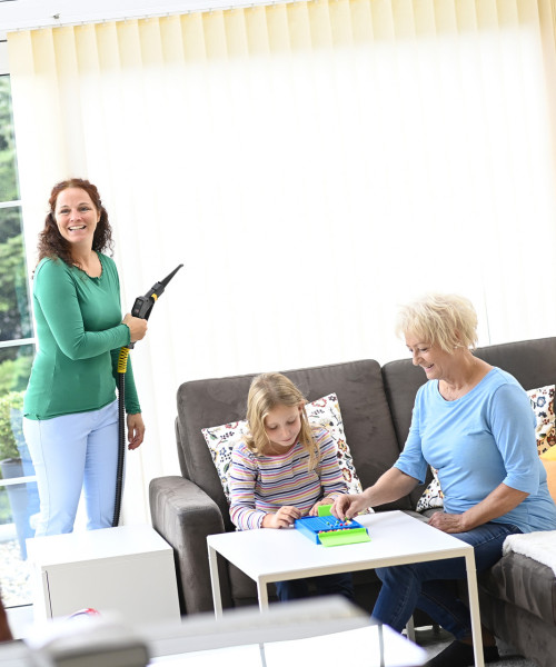 Famille heureuse dans le jardin d'hiver pendant que maman nettoie le rideau à lamelles avec la vapeur sèche Thermostar
