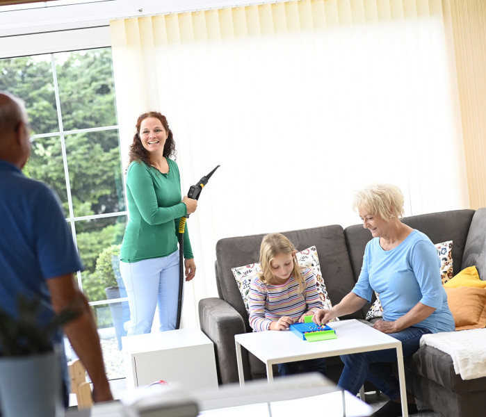 Famille heureuse dans le jardin d'hiver pendant que maman nettoie le rideau à lamelles avec la vapeur sèche Thermostar